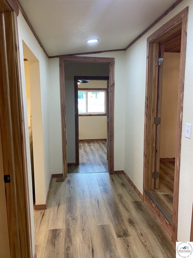 hall featuring a textured ceiling, baseboards, recessed lighting, ornamental molding, and wood finished floors