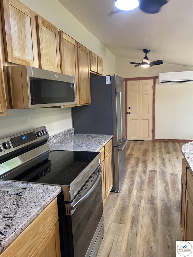 kitchen with light stone counters, a wall unit AC, appliances with stainless steel finishes, ceiling fan, and light wood-type flooring