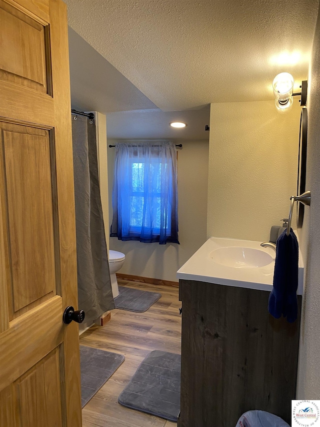 full bathroom featuring wood finished floors, a shower with shower curtain, toilet, vanity, and a textured ceiling