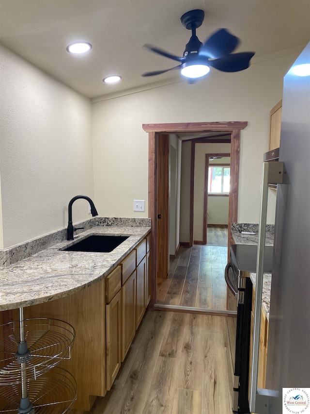 kitchen with light wood-style flooring, a sink, ceiling fan, electric range oven, and light stone countertops