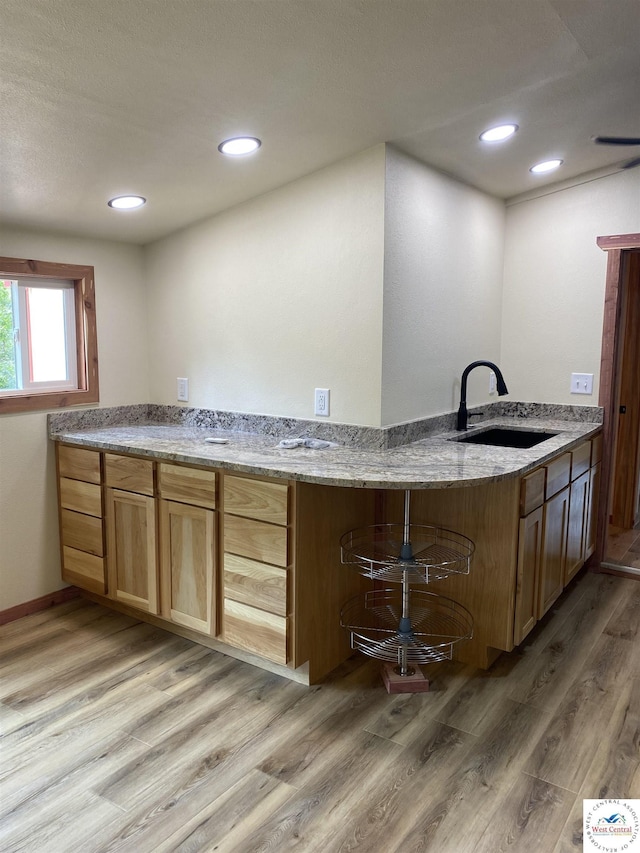 kitchen featuring light wood finished floors, recessed lighting, a sink, and light stone counters