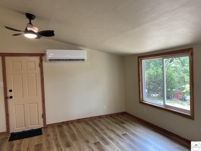 spare room featuring lofted ceiling, light wood-style flooring, baseboards, an AC wall unit, and a ceiling fan