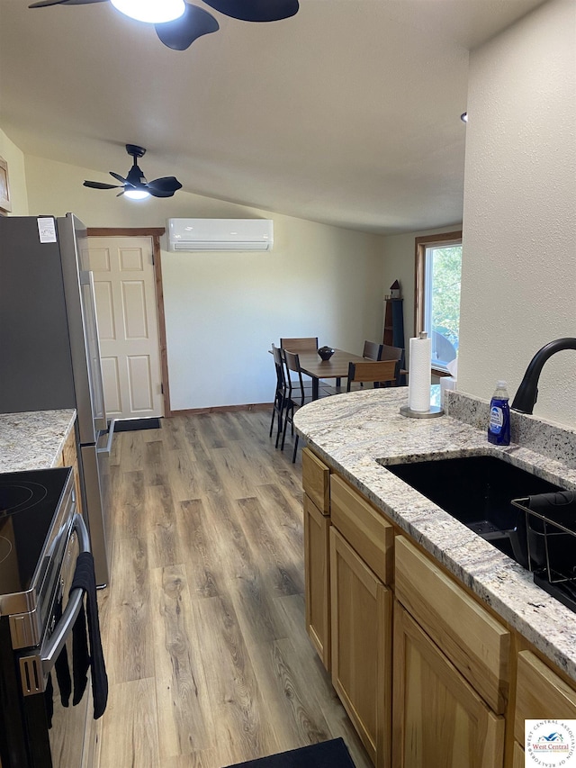 kitchen with light wood finished floors, light stone countertops, a sink, a wall mounted air conditioner, and a ceiling fan