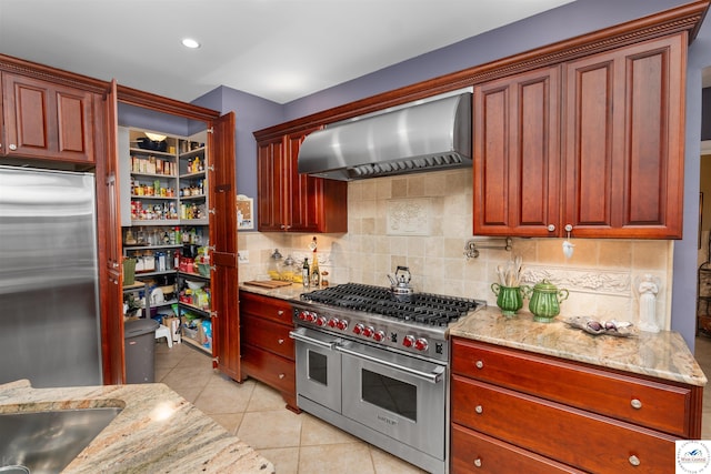 kitchen featuring decorative backsplash, light stone counters, light tile patterned floors, high quality appliances, and wall chimney exhaust hood