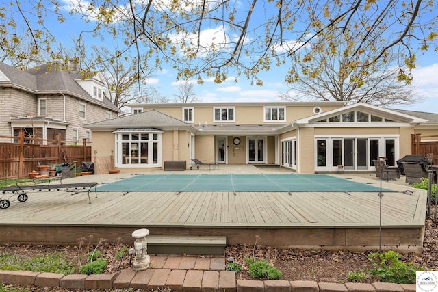 rear view of property featuring brick siding, fence, a fenced in pool, a wooden deck, and french doors