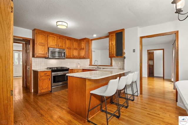 2105 Stonewood Cir, Sedalia, MO 65301 - kitchen featuring appliances with stainless steel finishes, brown cabinetry, light wood-type flooring, and a textured ceiling