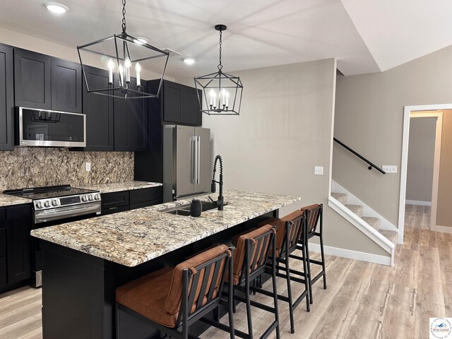 28927 Benton House Ave, Warsaw, MO 65355 - kitchen with a kitchen island with sink, a sink, a chandelier, light stone counters, and appliances with stainless steel finishes