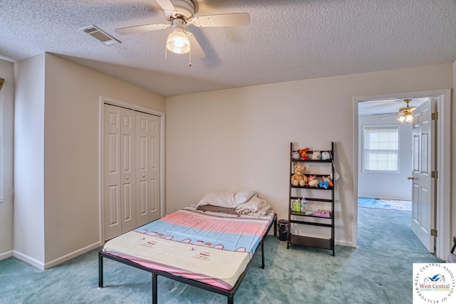 carpeted bedroom with a textured ceiling, visible vents, baseboards, and a closet