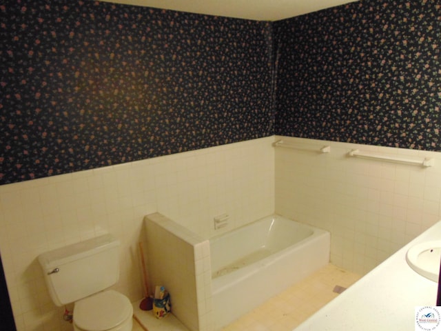 full bathroom featuring wallpapered walls, wainscoting, tile walls, toilet, and a bath