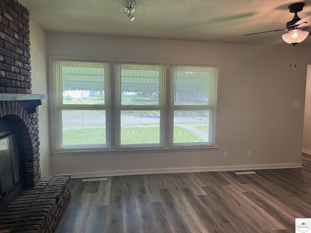 1404 S Grand Ave, Sedalia, MO 65301 - unfurnished living room with ceiling fan, a brick fireplace, a textured ceiling, wood finished floors, and visible vents