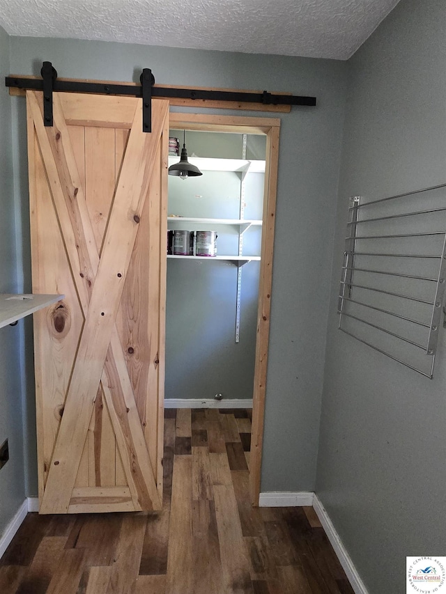interior space featuring a textured ceiling, baseboards, a barn door, and dark wood-type flooring