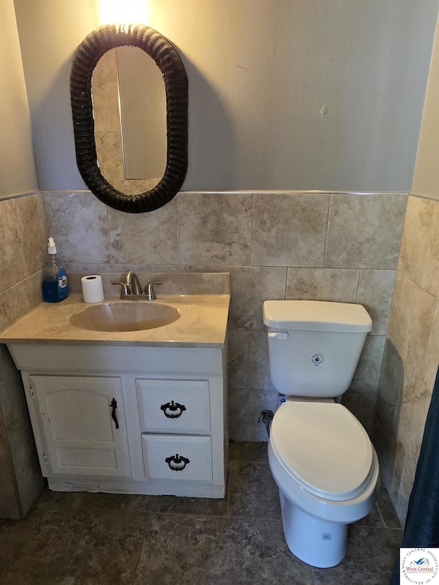 bathroom with toilet, vanity, a wainscoted wall, and tile walls