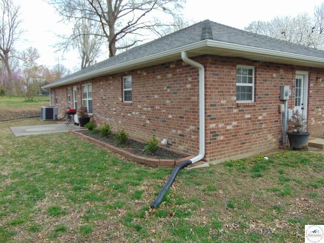 view of side of home with a lawn, a patio area, brick siding, and central AC unit