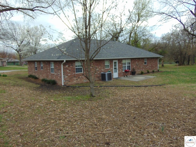rear view of house with a yard, brick siding, a shingled roof, central air condition unit, and a patio area