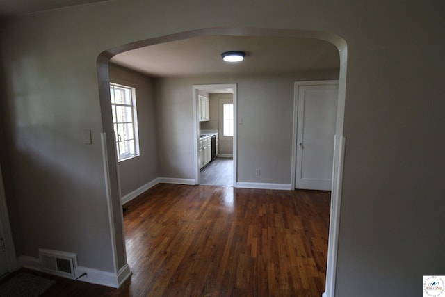 unfurnished dining area featuring baseboards, visible vents, arched walkways, and dark wood-type flooring