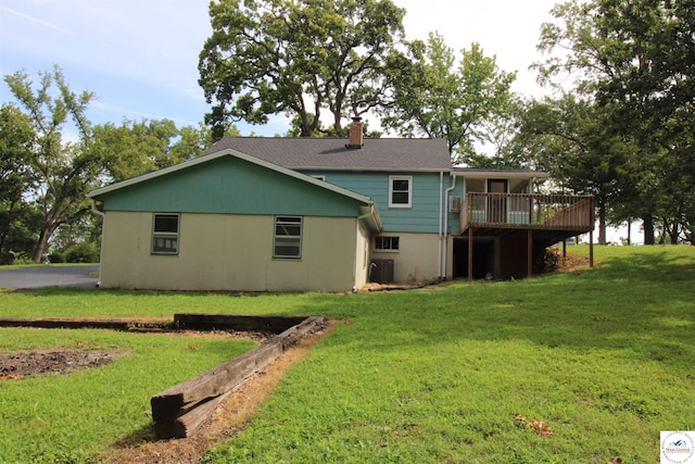 rear view of house with a chimney, a wooden deck, and a lawn