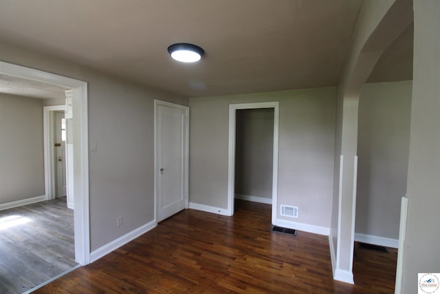 empty room with dark wood-style flooring, visible vents, and baseboards