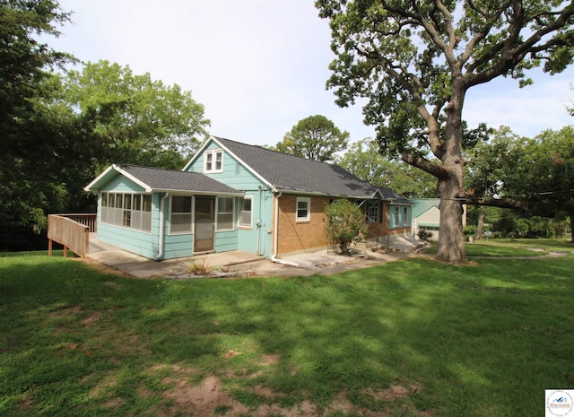 rear view of house with brick siding, a yard, a sunroom, and roof with shingles