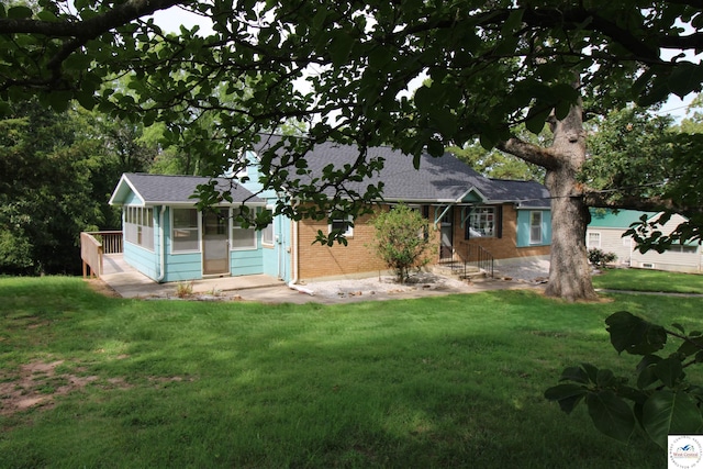 ranch-style house featuring roof with shingles, a front yard, brick siding, and a sunroom