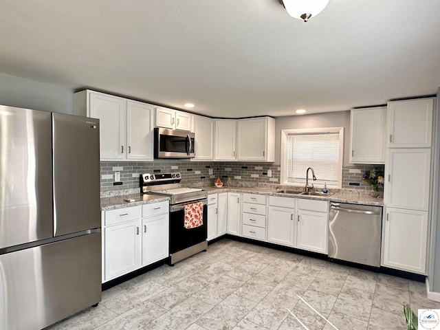 kitchen with light stone countertops, a sink, stainless steel appliances, backsplash, and white cabinetry