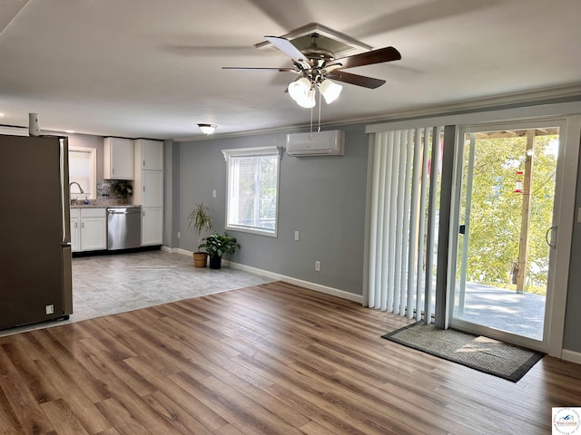 unfurnished living room featuring a sink, an AC wall unit, a ceiling fan, and baseboards