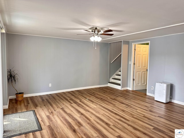 spare room with wood finished floors, a ceiling fan, baseboards, and stairs