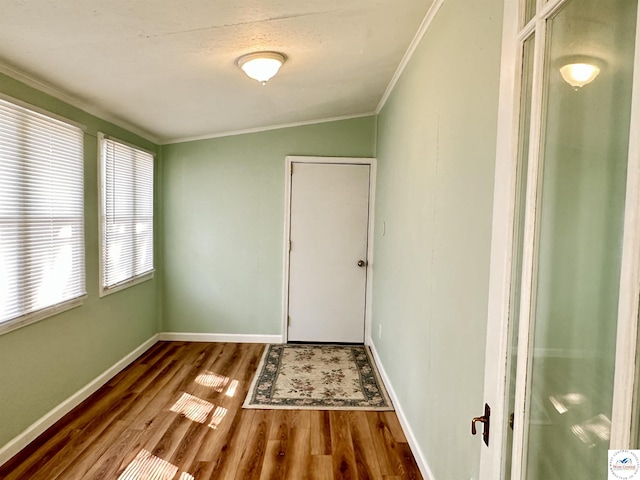 interior space with baseboards, wood finished floors, lofted ceiling, and crown molding