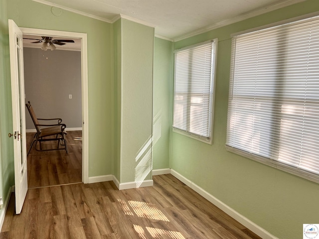 spare room with crown molding, a ceiling fan, wood finished floors, and baseboards