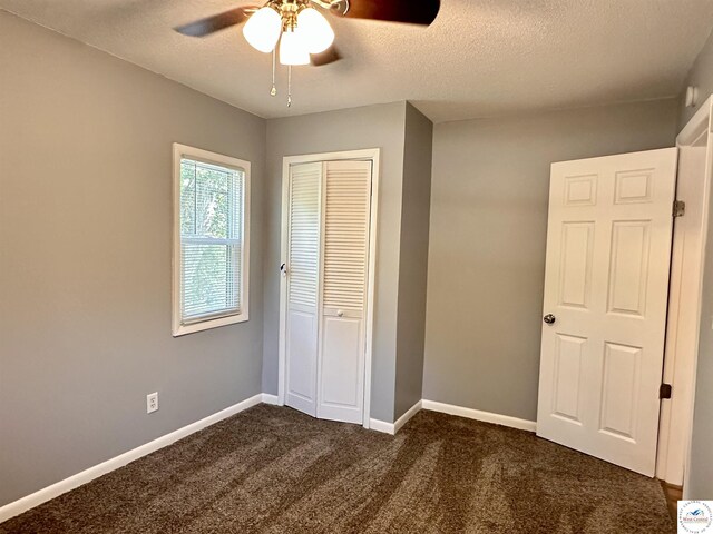 unfurnished bedroom with a closet, dark colored carpet, ceiling fan, baseboards, and a textured ceiling