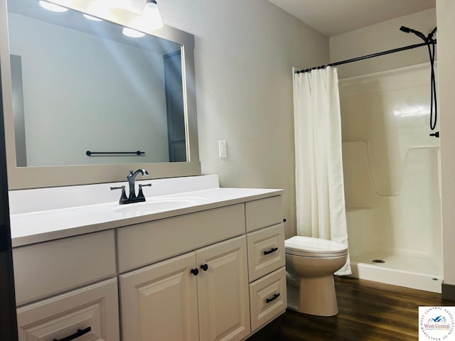 bathroom featuring wood finished floors, a shower stall, toilet, a textured wall, and vanity