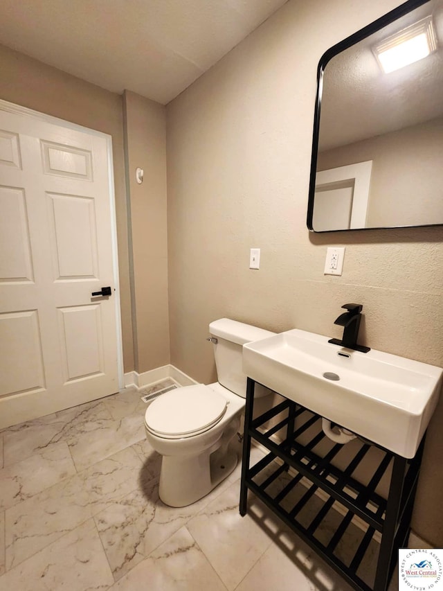 bathroom featuring toilet, marble finish floor, and a sink