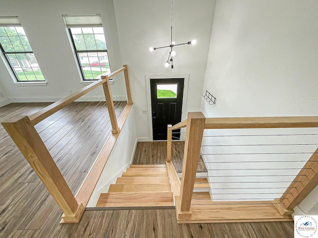 stairs featuring an inviting chandelier, baseboards, wood finished floors, and a wealth of natural light