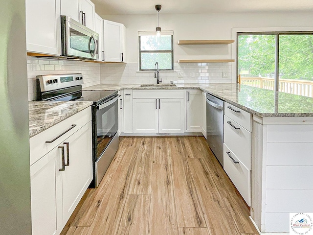 kitchen with decorative backsplash, appliances with stainless steel finishes, a sink, white cabinets, and light wood-style floors
