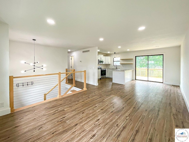 unfurnished living room with visible vents, baseboards, wood finished floors, and an inviting chandelier