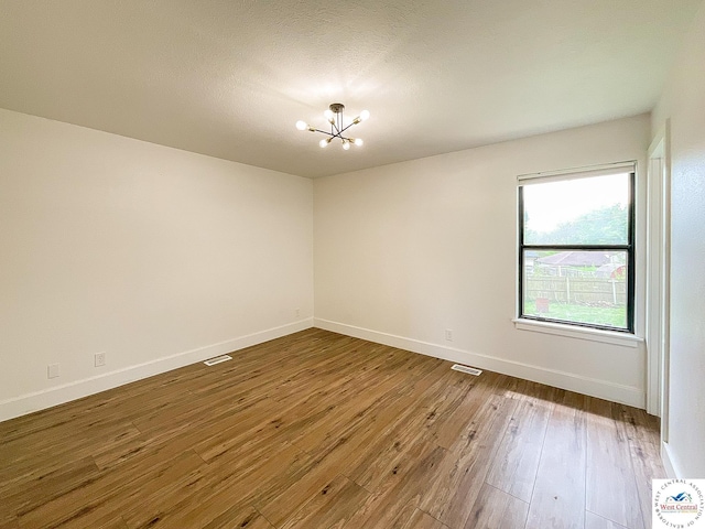 empty room featuring wood-type flooring, baseboards, a notable chandelier, and visible vents