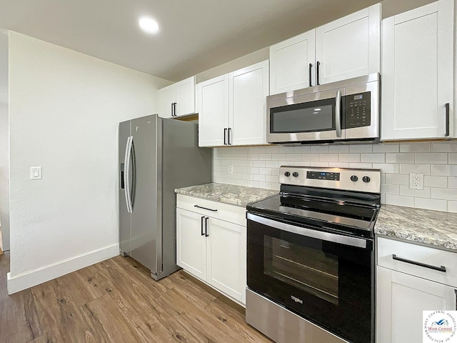 kitchen featuring white cabinets, light stone countertops, appliances with stainless steel finishes, light wood-style flooring, and tasteful backsplash