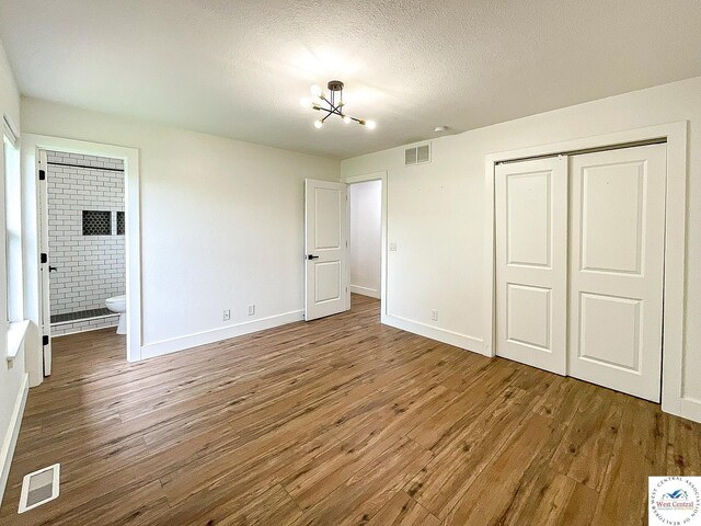 unfurnished bedroom featuring baseboards, a chandelier, wood finished floors, and visible vents