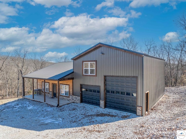 view of front of property with a porch, metal roof, a garage, driveway, and stone siding