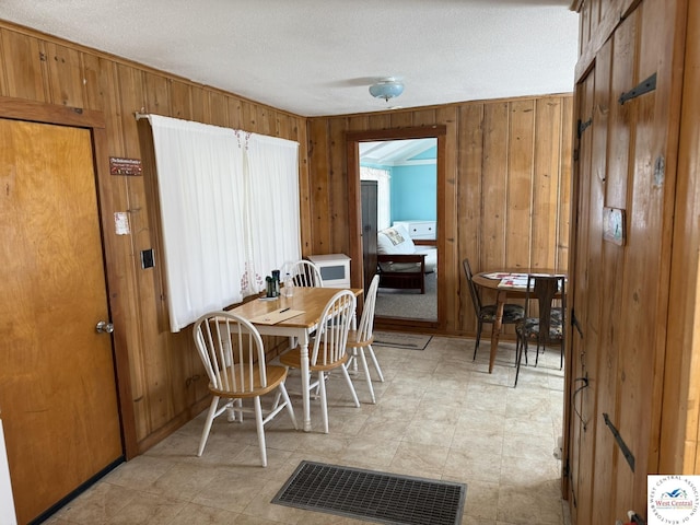 dining area with wooden walls, a textured ceiling, and visible vents
