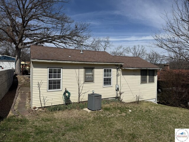 back of house featuring a lawn, central AC unit, and a shingled roof