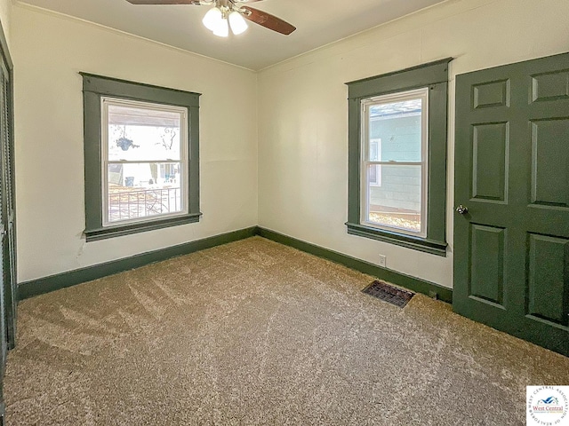 carpeted empty room with baseboards, visible vents, a ceiling fan, and crown molding