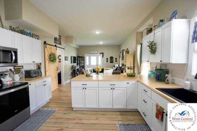 1625 W 16th St, Sedalia, MO 65301 - kitchen featuring stainless steel appliances, a peninsula, a barn door, white cabinets, and recessed lighting