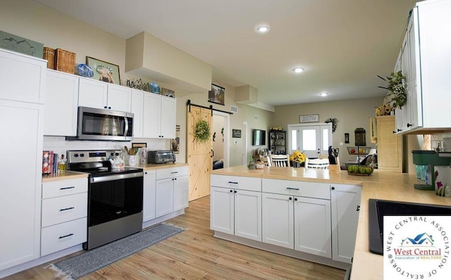 1625 W 16th St, Sedalia, MO 65301 - kitchen featuring stainless steel appliances, a peninsula, light countertops, white cabinets, and a barn door