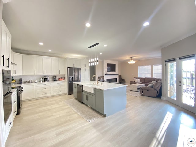 kitchen with light wood finished floors, a sink, black appliances, open floor plan, and white cabinetry