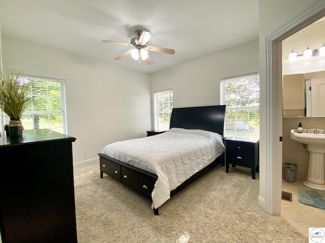 bedroom with light tile patterned floors, a ceiling fan, light carpet, baseboards, and ensuite bathroom