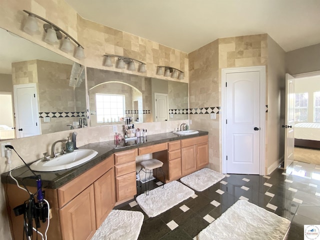 ensuite bathroom with a sink, ensuite bathroom, a wealth of natural light, and tile walls