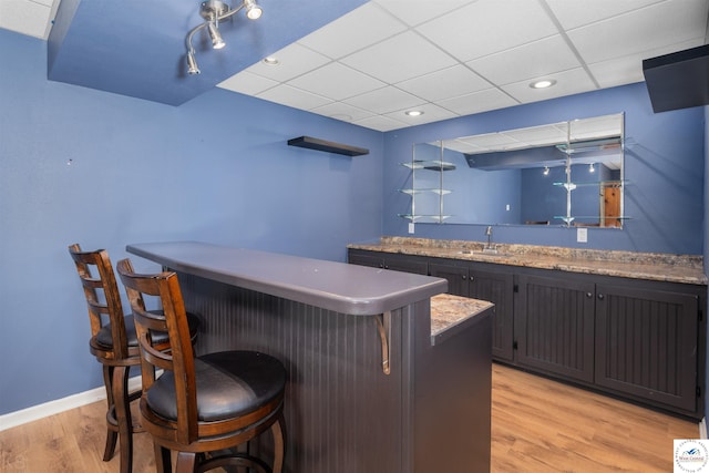 bar featuring a sink, baseboards, light wood finished floors, a paneled ceiling, and wet bar