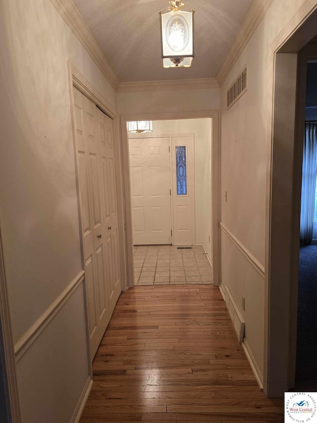 hall with a textured ceiling, visible vents, hardwood / wood-style flooring, and crown molding