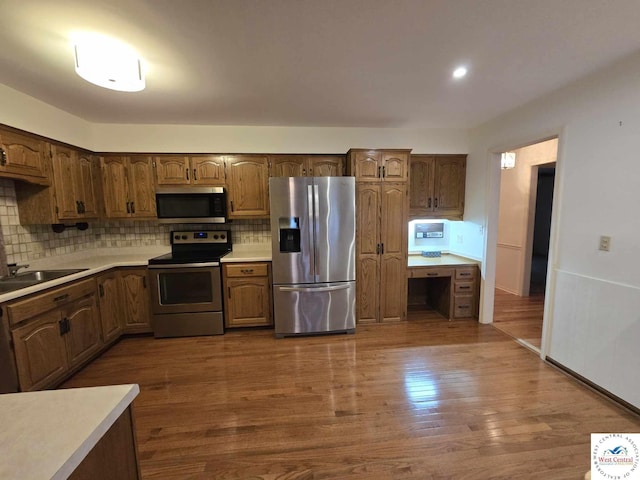kitchen featuring tasteful backsplash, a sink, stainless steel appliances, light countertops, and dark wood-type flooring