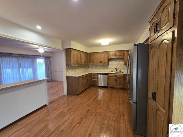 kitchen with a sink, stainless steel appliances, tasteful backsplash, light countertops, and wood finished floors
